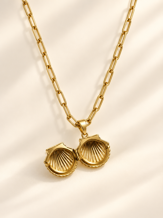 Gold scallop shell locket necklace with paperclip chain, shown open on a cream studio background